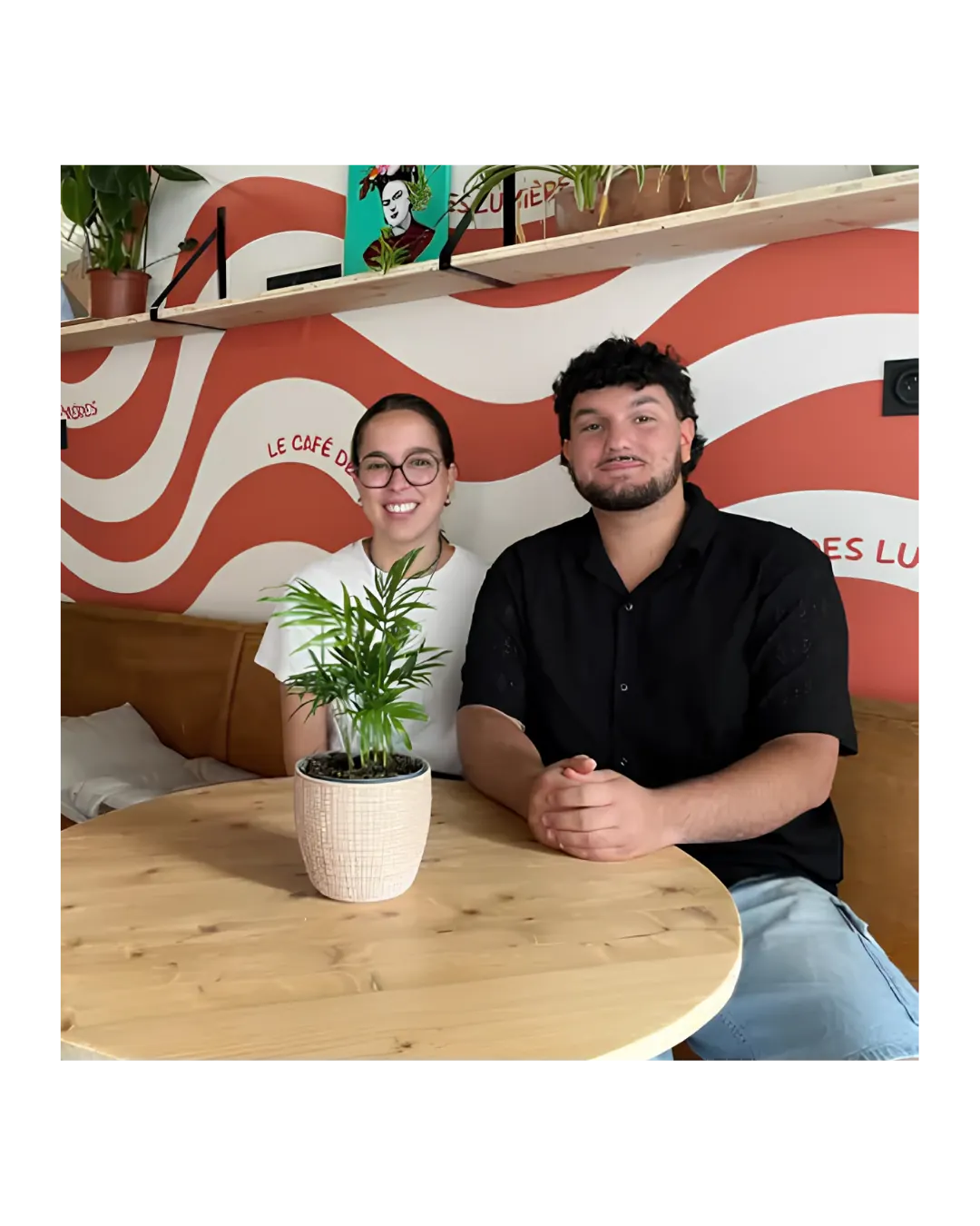 Léo et Mélia, fondateurs du Café des Lumières, attablés devant la fresque du café